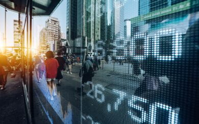 Digital stock market numbers reflect across a glass building façade in a busy financial district, symbolizing the fast-moving public company and securities landscape.