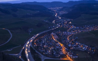 Aerial night view of a smart city with illuminated highways and neighborhood lights, illustrating “Connected Life” digital infrastructure, mobility, and IoT networks.